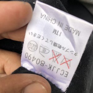 May include: A white tag with black text and symbols, including "MADE IN CHINA" and "ECJJK-80490". The tag also features Japanese text and care symbols, with a red "do not tumble dry" symbol.