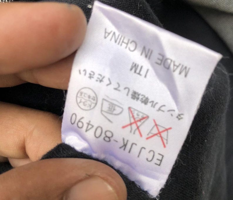 May include: A white tag with black text and symbols, including "MADE IN CHINA" and "ECJJK-80490". The tag also features Japanese text and care symbols, with a red "do not tumble dry" symbol.