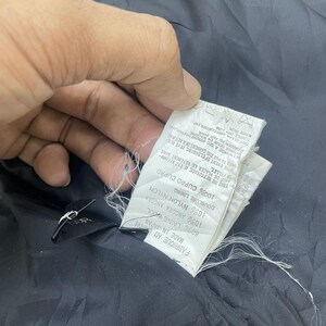 Puede incluir: Una etiqueta de tela negra con texto blanco que detalla la composici&oacute;n de la tela de la prenda. La etiqueta dice "Fabrique au Japan, Made in Japan, 80% Laine Wool, 10% Angora Angora, Doublure Lining, 10% Nylon Nylon, 100% Cupro Cupro".