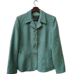May include: A teal blazer with a classic design, featuring a notched collar, two front pockets, and four button closures. The blazer is hanging on a wooden hanger against a white background. The label reads "Max Mara".