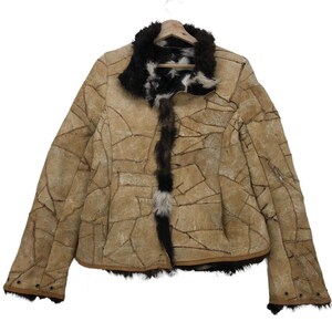 May include: A tan leather jacket with a patchwork design. The jacket features a black fur collar and trim, with a brown fur accent down the front. The jacket is hanging on a wooden hanger.