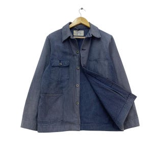 May include: A blue corduroy jacket with a button-up front, two chest pockets, and two lower pockets. The jacket is hanging on a wooden hanger against a white background. The jacket has a collar and long sleeves.