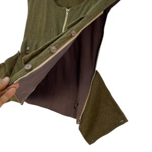 May include: Olive green vest with a brown interior. The vest features a zipper closure, wooden buttons, and small pockets. The interior lining is a solid brown color. The vest is made of a textured fabric.