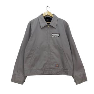 以下が含まれることがあります： 襟付き、ジッパー開閉のグレーのワークジャケット。 ジャケットにはフロントポケットが2つあり、「ENGINEERING」と書かれた小さなパッチが付いています。 Dickiesのロゴが右下に表示されています。