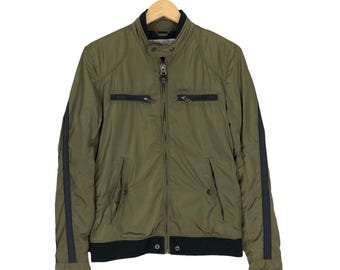 May include: Olive green jacket with black accents and a full-length zipper. Features black stripes down the sleeves and a black band at the waist. The jacket has two zippered chest pockets and a stand-up collar.