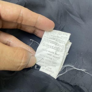 Puede incluir: Una etiqueta de tela negra con texto blanco que detalla la composici&oacute;n de la tela de la prenda. La etiqueta dice "Fabrique au Japan Made in Japan 3 80% Laine Wool 10% Angora Amora Doublure Lining 10% Nylon Nylon 100% Cupro Cupro On Fillet Ande de Placer le Vetement dans The Event of Cleaning, It is Req Need to Put the Carment in Anet Mag Yoyage a Seo Prometruthylene Passeriad F Dry Clean Warm Iron"