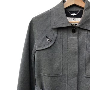 May include: A gray coat with a notched collar and a button closure. The coat has two front pockets and a small decorative button on the left side. The coat is hanging on a wooden hanger.
