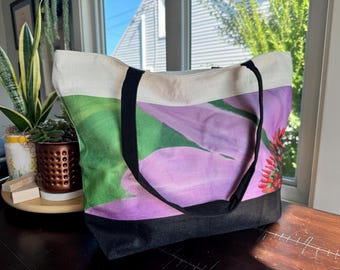 May include: A large canvas tote bag with black straps. The bag features a floral print with pink, green, and red colors.