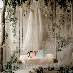 May include: A newborn baby is sleeping on a white faux fur swing hanging from a tree branch. The swing is decorated with greenery and a white sheer curtain.
