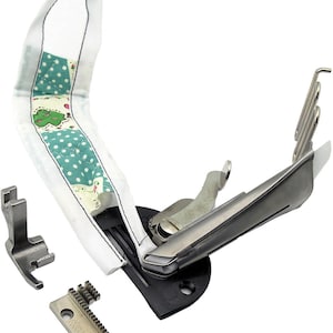 May include: A silver sewing machine attachment for creating rolled hems. The attachment has a metal foot, a guide, and a spring-loaded needle. A piece of fabric is threaded through the attachment, showing how it works.
