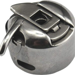 Könnte beinhalten: Ein silbernes Metall-Spulenkapsel mit einem Hebel zum Aufwickeln von Garn. Die Spulenkapsel ist für die Verwendung mit Nähmaschinen konzipiert.