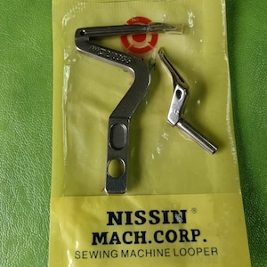 May include: A set of sewing machine loopers in a yellow plastic package. The package has the text "NISSIN MACH.CORP. SEWING MACHINE LOOPER". The loopers are silver-colored metal and appear to be new.