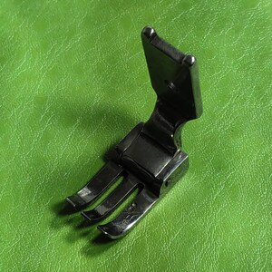 Peut inclure: Un pied de machine à coudre en métal noir avec trois pointes. Le pied est conçu pour coudre le cuir ou d'autres tissus épais.