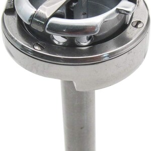May include: A silver sewing machine bobbin case with a metal hook and a silver metal post.