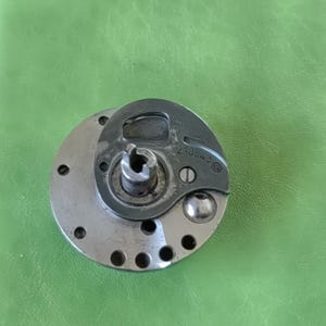 以下が含まれることがあります： 銀色と黒色の金属製のミシン部品のクローズアップ。部品には「210342」という番号が印刷されています。