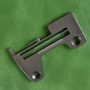 Peut inclure: Un pied de machine à coudre en argent avec une rainure pour le passage du fil. Le pied a deux trous sur le dessous.