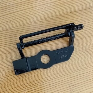 Könnte beinhalten: Schwarzes Metallteil mit einem Zahnradmechanismus und einem runden Loch. Das Teil ist mit "PPAF" und "20083X45" beschriftet.