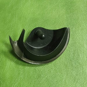 Pode incluir: Um pé de máquina de costura preto com forma curva e um pequeno pino de metal no centro.
