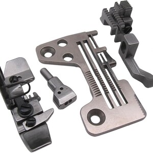 Könnte beinhalten: Eine Sammlung von silberfarbenen Nähmaschinen-Teilen, darunter Nähfüße und andere Aufsätze. Die Komponenten sind aus Metall gefertigt und für verschiedene Nähfunktionen konzipiert. Das Bild zeigt eine Vielzahl von Formen und Größen, die für verschiedene Nähaufgaben geeignet sind.