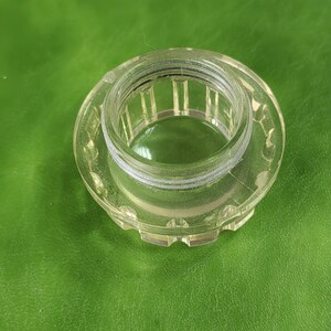 以下が含まれることがあります： 透明な円形のボトルストッパー。内側はネジ山があり、装飾的なスカラップエッジが付いています。ストッパーは透明な素材でできており、光を通します。デザインはシンプルで機能的です。