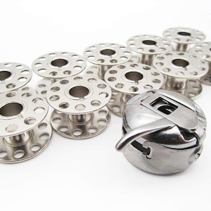 Può includere: Un set di dieci bobine argentate per una macchina da cucire, con un avvolgitore di bobine argentato.