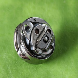 以下が含まれることがあります： 金属製のフックと小さな金属製のボールベアリングが付いた銀色のミシンボビンケース