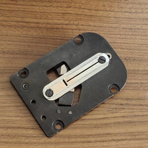 Può includere: Un pezzo di macchina da cucire in metallo nero con uno slider in metallo argentato. Lo slider ha una piccola scanalatura al centro.