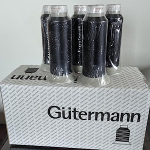 以下が含まれることがあります： 箱に「Gütermann」というブランド名が印刷された黒い糸の糸巻きが4つあります。