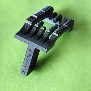 Könnte beinhalten: Nahaufnahme von zwei schwarzen Metall-Haarschneidemaschinenklingen mit kammartigem Design. Die Klingen liegen auf einer grünen Oberfläche. Der Text "35605BRW6 U" ist auf dem Griff der unteren Klinge aufgedruckt.