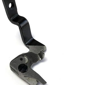 Könnte beinhalten: Ein schwarzer Nähmaschinen-Nähfuß aus Metall mit geschwungenem Design und einem kleinen Loch oben. Der untere Teil ist silberfarben und hat ein scharnierartiges, abgewinkeltes Design mit einer kleinen, schwarzen Schraube.