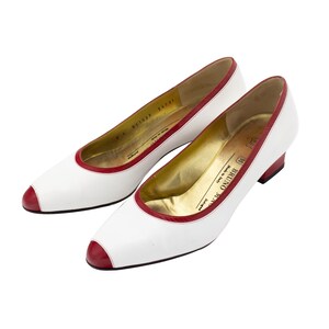 May include: A pair of white leather pumps with red trim and a low heel. The shoes are made in Italy by Bruno Magli.