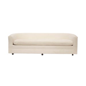 May include: A white curved sofa with a tufted back and a simple design. The sofa is on wheels and has a light beige fabric upholstery.