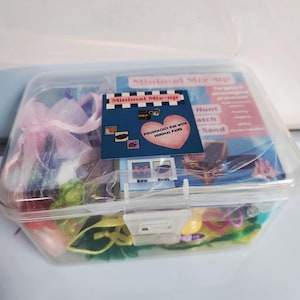 May include: A clear plastic container labeled "Minimal Mix-up" holds various small, colorful items. A card with a pink heart and the text "Phonology Fun with Minimal Pairs" is visible. The container is filled with toys and accessories.