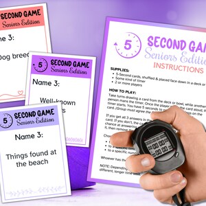 May include: A printable party game titled Second Game Seniors Edition, featuring an instruction sheet and three prompt cards with the text Name 3: Dog breeds, Well-known fruits, and Things found at the beach, alongside a black digital stopwatch.