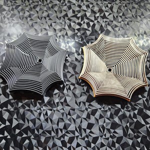Könnte beinhalten: Zwei dekorative Metallobjekte mit geometrischem Design. Das Objekt links ist schwarz und das Objekt rechts ist golden. Beide Objekte befinden sich auf einer schwarz-weißen gemusterten Oberfläche.