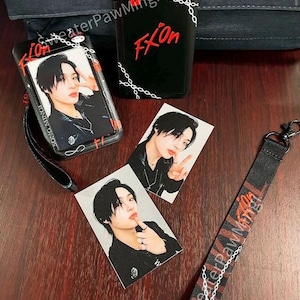 May include: A black plastic ID badge holder with a chain pattern and red text reading FXion, two rectangular photo cards featuring a person with black hair, and a black fabric lanyard with red and white chain graphics and the text SweaterPawMing.