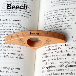 May include: A beechwood book page holder with the name "Laura" engraved. The wooden bookmark features floral and butterfly designs. The holder is designed to slip over a finger for easy reading.