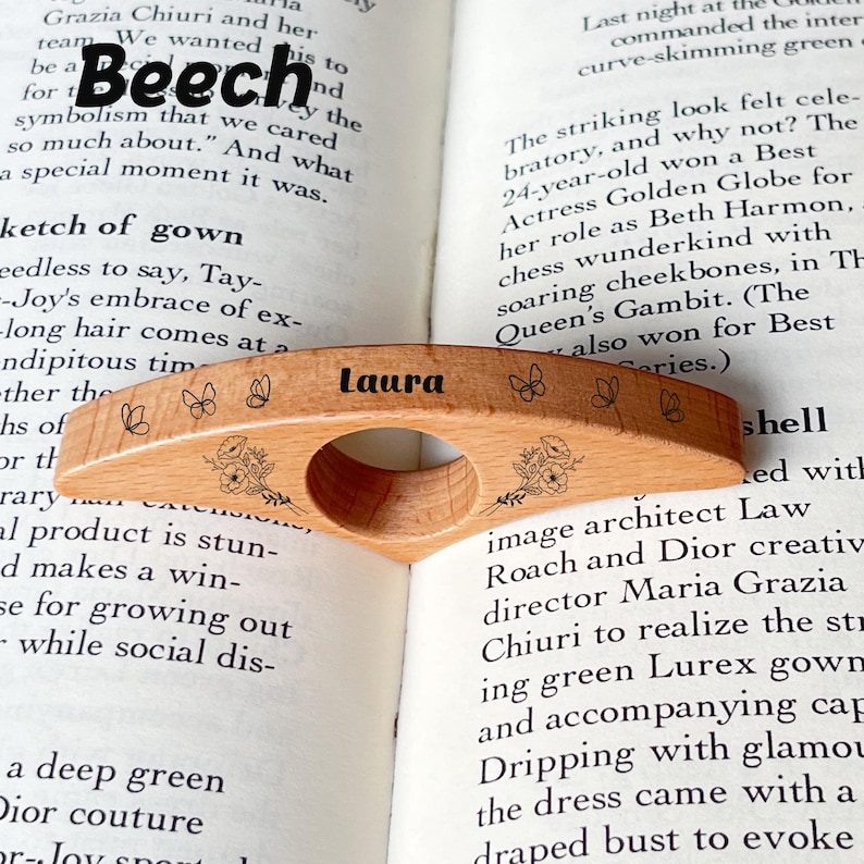 May include: A beechwood book page holder with the name "Laura" engraved. The wooden bookmark features floral and butterfly designs. The holder is designed to slip over a finger for easy reading.