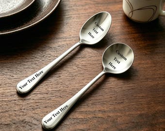 Könnte beinhalten: Zwei polierte, silberfarbene Metalllöffel mit glatten, abgerundeten Griffen. Jeder Löffel trägt den schwarz gravierten Text Custom Text Here auf der Laffe und Your Text Here auf dem Griff, was die anpassbare Oberfläche deutlich zeigt.