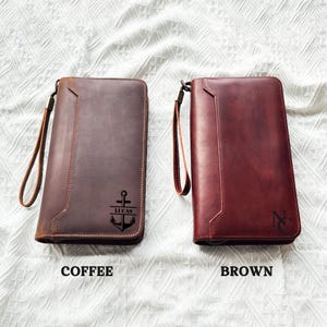 May include: Two leather wallets, one coffee-colored and one brown, with wrist straps. The coffee-colored wallet has an anchor design and the name "LUCAS". The brown wallet has the initials "N".