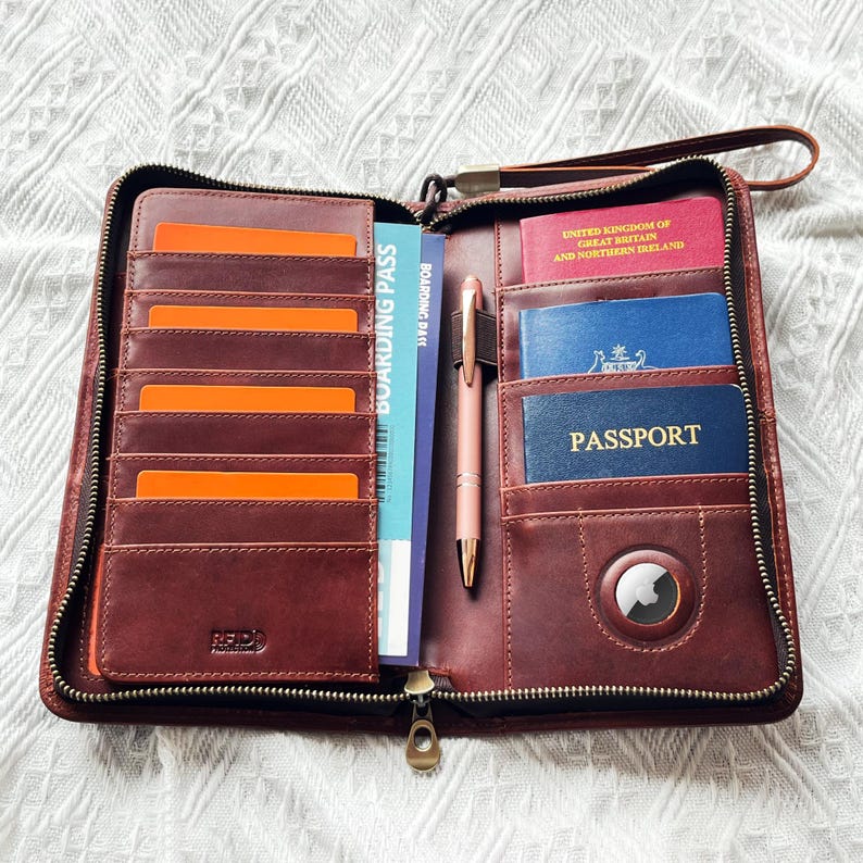May include: Open brown leather travel wallet with multiple card slots, a boarding pass, and a pen. The wallet contains a passport and other documents. A wrist strap and zipper closure are visible.