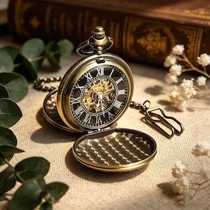 May include: An open antique pocket watch with a bronze-coloured case and a black face featuring Roman numerals. The watch reveals its intricate inner workings. A chain and clasp are attached. The watch is set against a neutral background.
