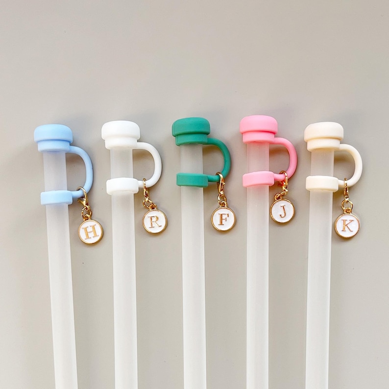 May include: Five clear plastic straws with colorful toppers in blue, white, green, pink, and cream. Each straw has a matching handle and a gold charm with a letter. The letters are H, R, F, J, and K.