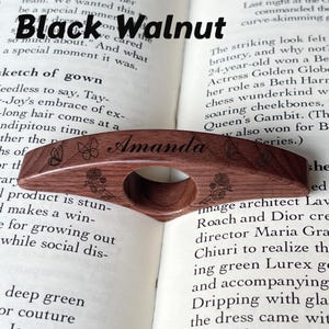 May include: A black walnut wood page holder with the name "Amanda" engraved. The holder features butterfly and floral designs. The text "Black Walnut" is above the holder.