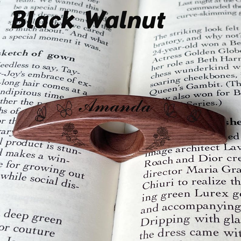 May include: A black walnut wood page holder with the name "Amanda" engraved. The holder features butterfly and floral designs. The text "Black Walnut" is above the holder.