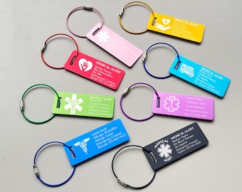 May include: A collection of eight rectangular medical alert tags in various colors, each attached to a circular metal wire ring. The tags feature printed medical information, emergency contact details, and symbols like the Star of Life.