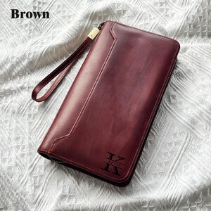May include: A brown leather wallet with a wrist strap and a zipper closure. The wallet has a smooth surface and features the name "KEVIN" with the letter "K" in a stylized font. The word "Brown" is in the top left corner.