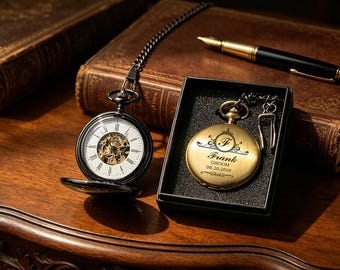 May include: Two pocket watches, one open, showing the internal mechanism, and the other in a black box. The open watch has a black case and a chain. The other watch is gold with the name "Frank" and the date "08.20.2026" engraved.