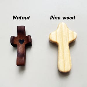 May include: Two wooden crosses, one walnut with a heart, the other pine. The walnut cross is dark brown with a black heart. The pine cross is light tan. The words "Walnut" and "Pine wood" are above each cross.