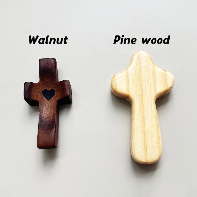 May include: Two wooden crosses, one walnut with a heart, the other pine. The walnut cross is dark brown with a black heart. The pine cross is light tan. The words "Walnut" and "Pine wood" are above each cross.